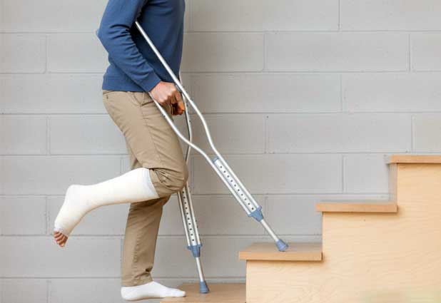 Man with a leg cast using crutches to go up a staircase.