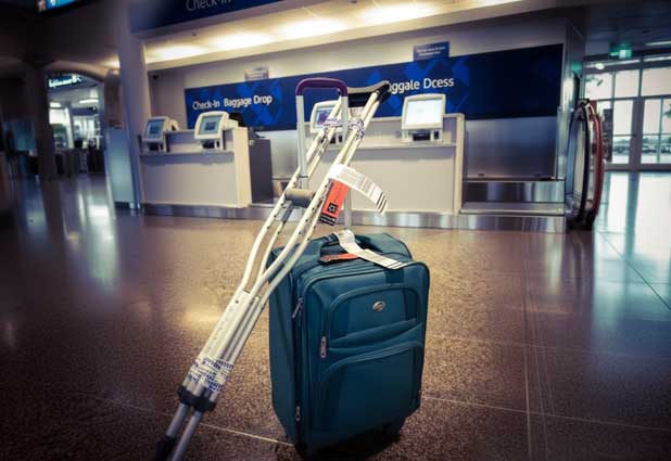 Traveler on crutches waiting at the airport with a backpack and carry-on.