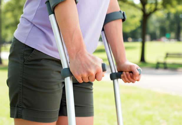 Close up of a person gripping forearm crutches while walking outdoors.